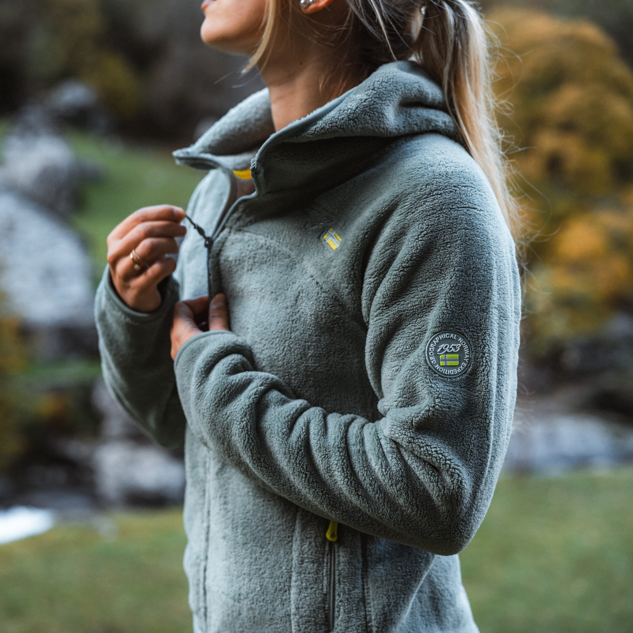Frau, die eine Geographical Norway Fleecejacke trägt und die Natur im Freien genießt. Ein warmes und bequemes Kleidungsstück, das sich ideal für Outdoor-Abenteuer eignet.
